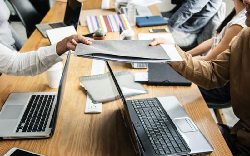 table of people with open laptops exchanging documents