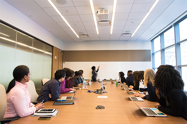 woman presenting to a boardroom full of watchers